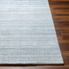 Light blue Surya Fresno area rug with subtle textured stripes on a dark wood floor.