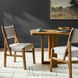 Two Surya Bergene dining chairs with light beige upholstery and brown rubber wood frames around a wooden table.