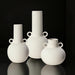 Three white ceramic decorative vases with sculptural, modern designs and small handles.