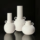 Three white ceramic decorative vases with sculptural, modern designs and small handles.