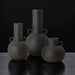 Set of three dark gray ceramic decorative vases with sculptural, globally inspired designs.