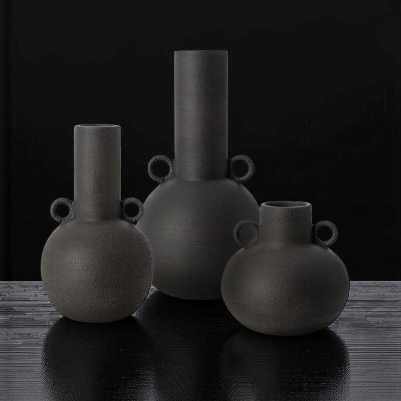 Set of three dark gray ceramic decorative vases with sculptural, globally inspired designs.