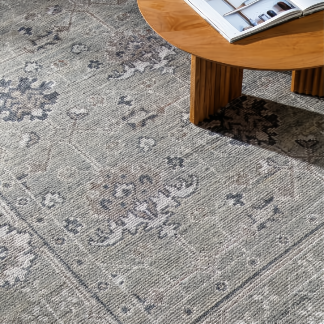 Surya Almeria low pile area rug in muted green with traditional floral patterns, next to a wooden table.