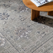 Surya Almeria low pile area rug in muted green with traditional floral patterns, next to a wooden table.