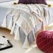 Cream Surya Dallan cotton throw with Moroccan-inspired pattern and tassels draped over a bed.