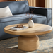 Beige mango wood round coffee table with a minimalist design, brushed finish, and sturdy base, styled in a living room.