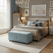 Light blue upholstered Surya Andra Ottoman at the foot of a bed in a stylish bedroom.