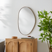 Modern organic-shaped wall mirror with a thin gold frame, hanging above a light wood cabinet.