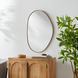 Modern organic-shaped wall mirror with a thin gold frame, hanging above a light wood cabinet.