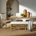 Surya Cape Town dining chair with white Sunbrella cushion, wheat aluminum frame, and matching bench on a jute rug.
