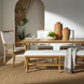 Surya Cape Town dining chair with white Sunbrella cushion, wheat aluminum frame, and matching bench on a jute rug.