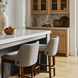Two Surya Brooke counter stools with medium brown polyester seats and wheat-finished beechwood bases in a kitchen.