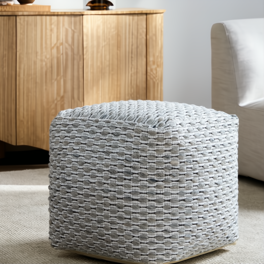 Gray woven wool cube pouf with textured stitched detailing on a light rug.