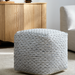 Gray woven wool cube pouf with textured stitched detailing on a light rug.