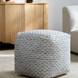 Gray woven wool cube pouf with textured stitched detailing on a light rug.