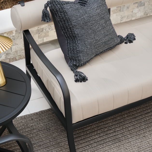 Surya Antibes outdoor sofa with beige Sunbrella upholstery, black aluminum frame, and a dark gray throw pillow.