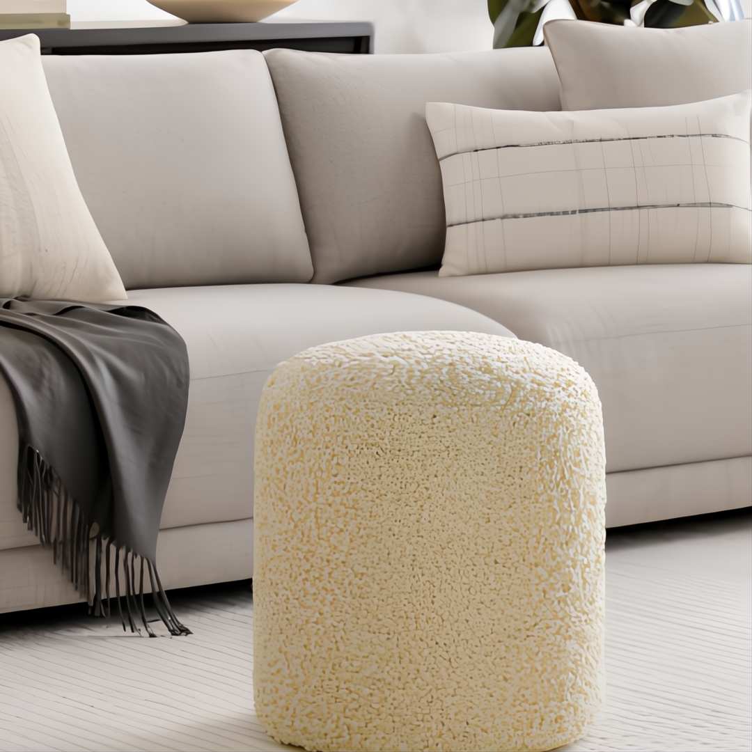 Cream Surya Mohave pouf with a textured woven polyester cover, cube shape, next to a light gray sofa.