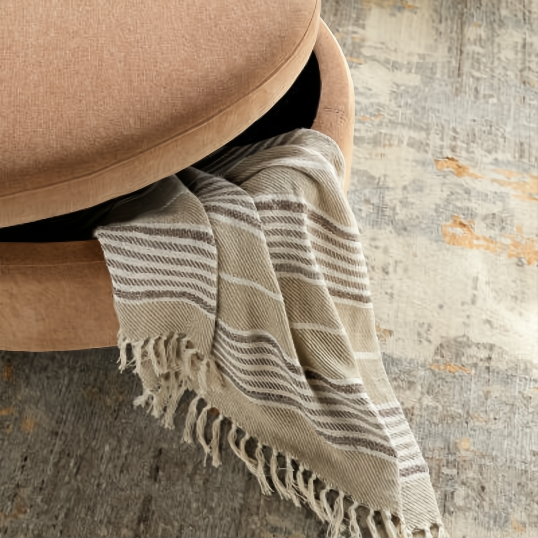 Brown and peach upholstered storage ottoman with a striped throw blanket partially visible.