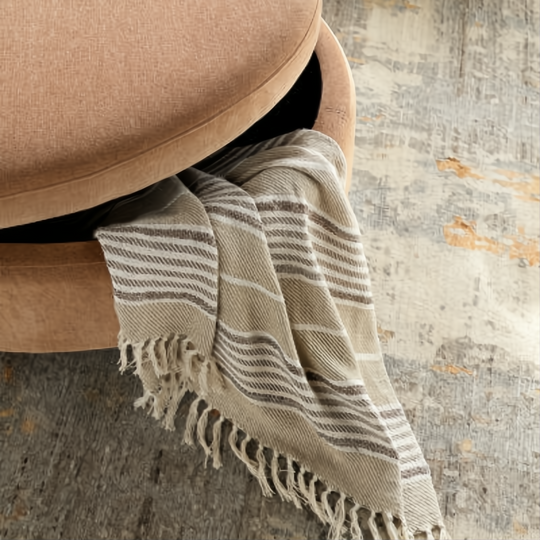 Brown and peach upholstered storage ottoman with a striped throw blanket partially visible.