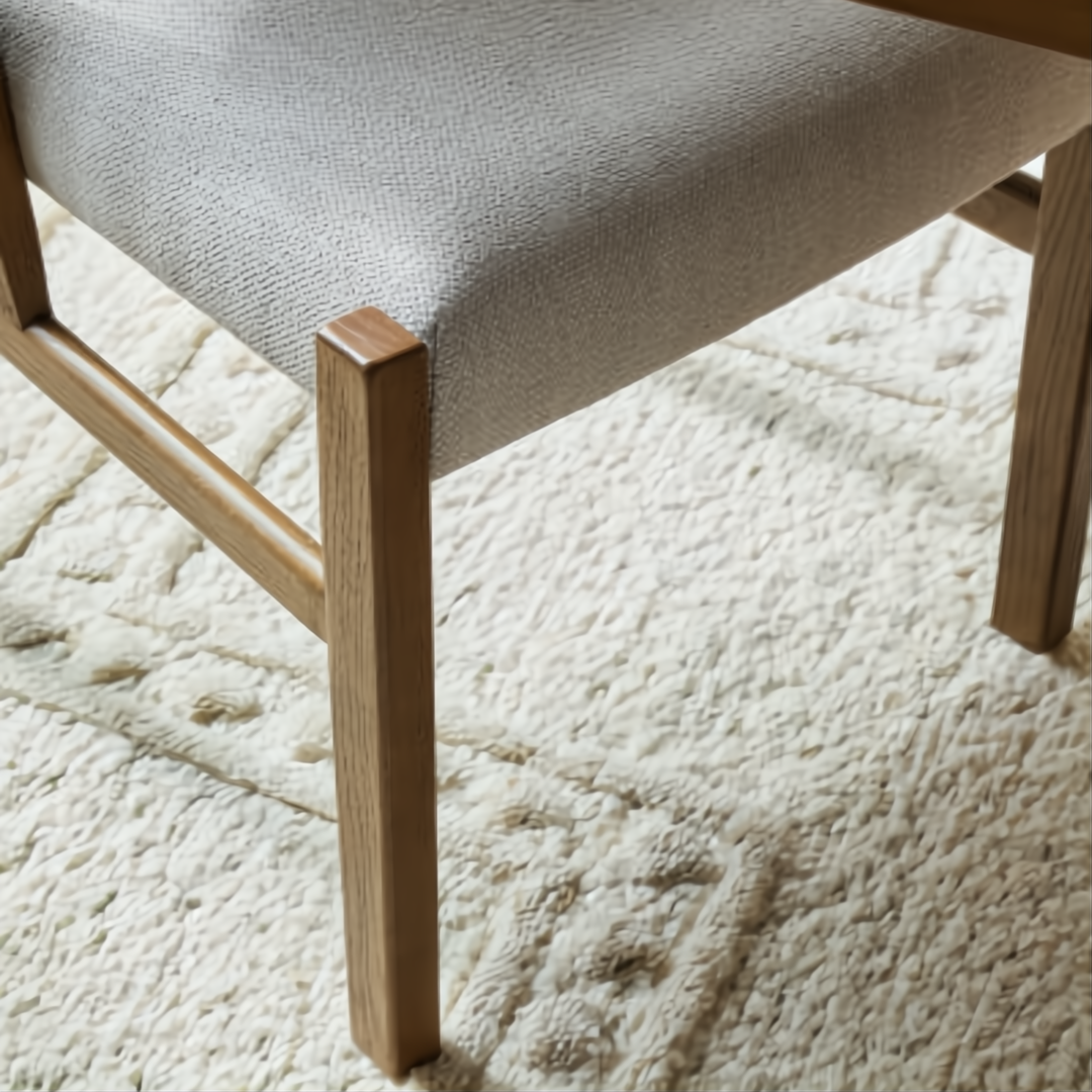 Surya Bergene dining chair with light beige upholstery and brown rubber wood legs on a textured rug.