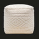 Surya Matthew Pouf, a cream knitted pouf with intricate beaded geometric patterns, on a dark background.