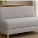 Light gray upholstered banquette bench with natural ash wood legs on a woven rug.