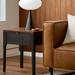 Brown Surya Anello end table with oak veneer top, dark drawer, and black legs next to a tan leather sofa.