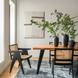 Modern dining room with black ceramic vases holding greenery on a wooden table, surrounded by black cane chairs.