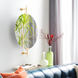 Modern oval mirror with gold-finished wall mounts, reflecting a plant, above a blue sofa and decorative vases.