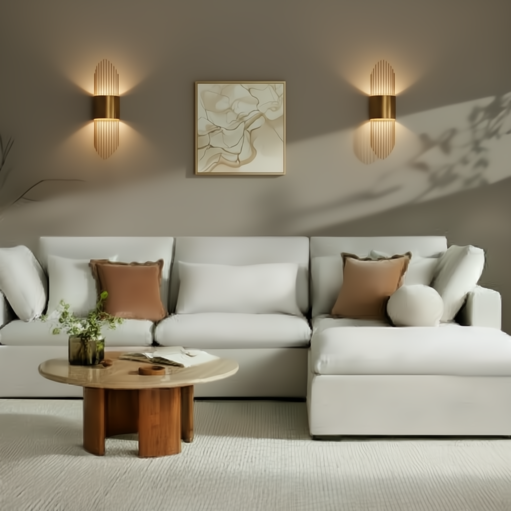 White sectional sofa with brown pillows, a round wooden coffee table, and gold wall sconces.