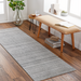 Surya Hickory HCK2303 gray multi-tone hand-loomed recycled PET yarn runner rug on a wood floor.