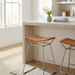 Modern counter stool with a brown leather saddle seat and metallic bronze iron base in a bright kitchen.
