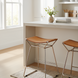 Modern counter stool with a brown leather saddle seat and metallic bronze iron base in a bright kitchen.
