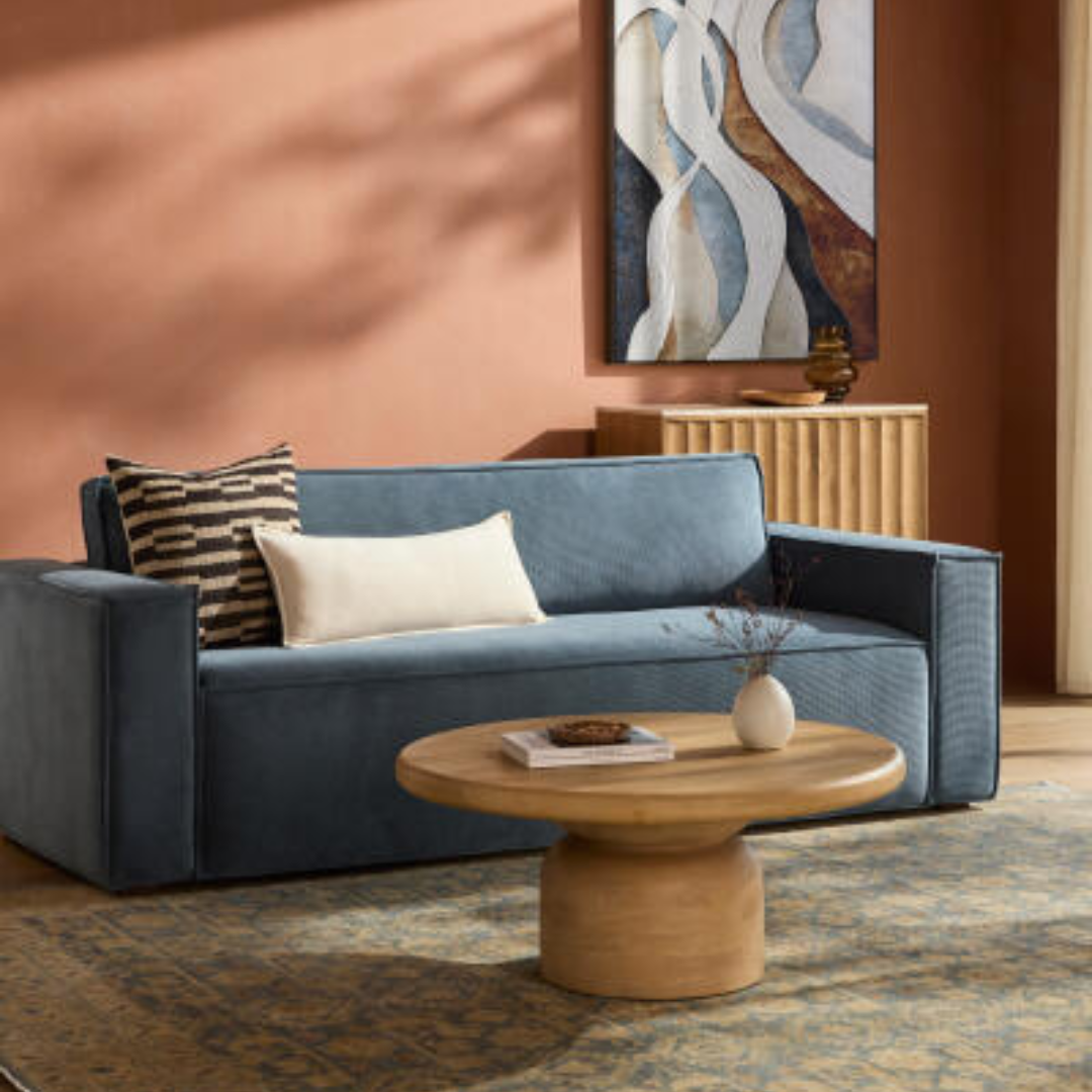Contemporary Surya Aira navy polyester sofa with a brown rubber wood base, styled with pillows and a coffee table.