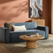 Contemporary Surya Aira navy polyester sofa with a brown rubber wood base, styled with pillows and a coffee table.