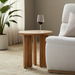Brown lacquered mango wood round end table with zigzag fluted legs next to a cream armchair.