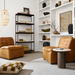 Two brown leather modular chairs with black bases in a contemporary living room with white shelves.
