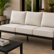 Surya Fairborn 83-inch outdoor sofa with black frame and light beige cushions on a patio.