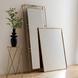 Two Surya Alchemist rectangular wall mirrors with hammered gold iron frames, one tall, one shorter, beside a plant on a gold side table.