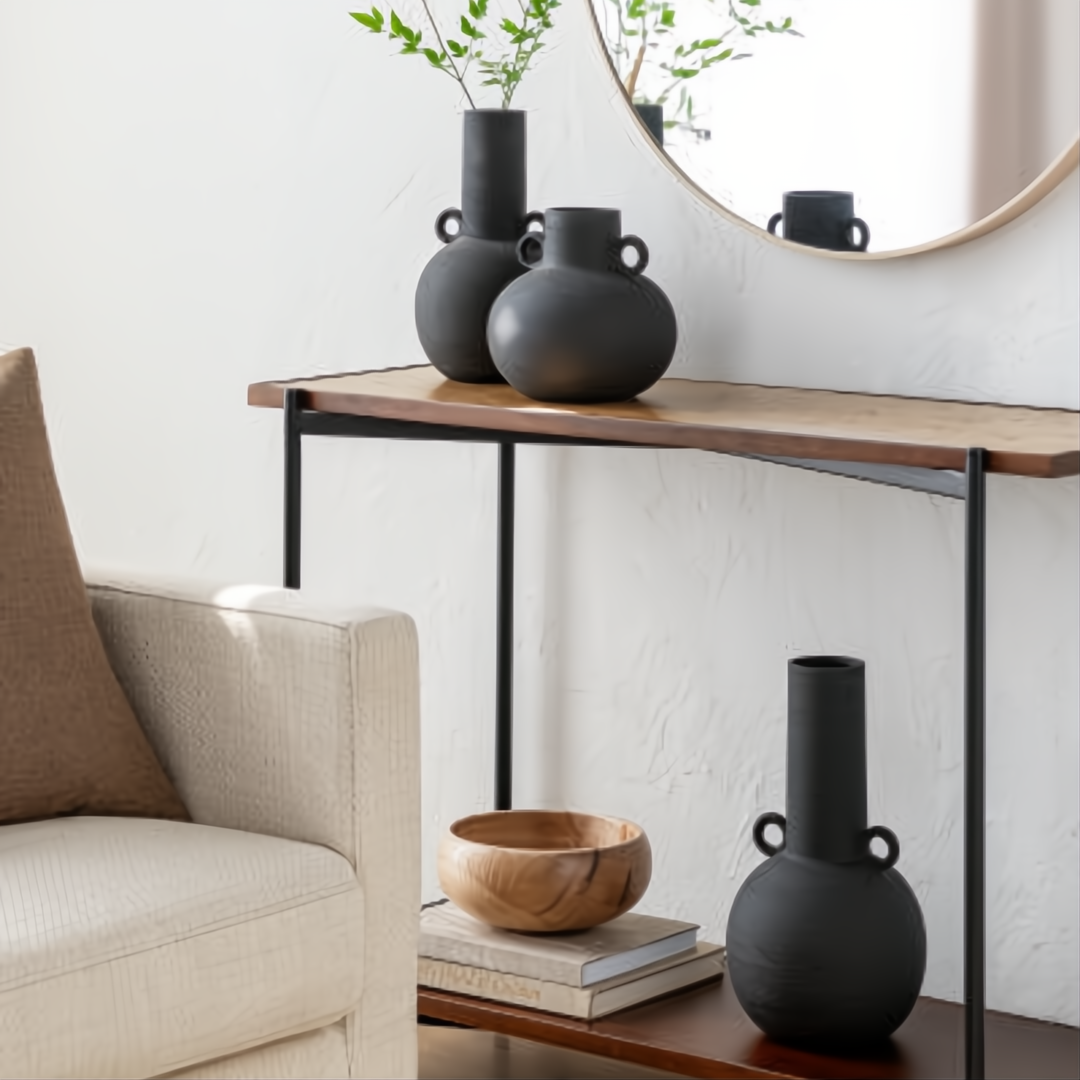 Modern black ceramic decorative accent set with sculptural vase forms on a console table.