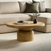 Beige mango wood round coffee table with a brushed finish, featuring a thick top and a cylindrical base.