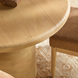 Beige round mango wood dining table with a brushed finish, next to a chair on a patterned rug.