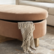 Brown and peach upholstered oval storage ottoman with a fringed throw blanket.