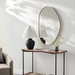 Modern gold-framed organic shaped wall mirror above a console table with lamp and vase.
