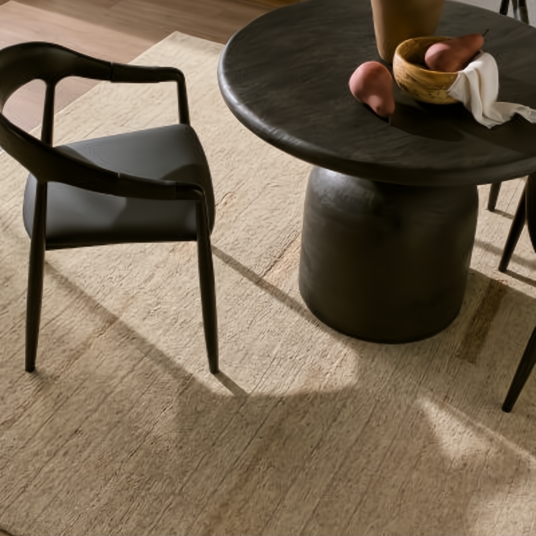 Surya Koben 39" round black sandblasted mango wood dining table with sculptural base and chair on a rug.