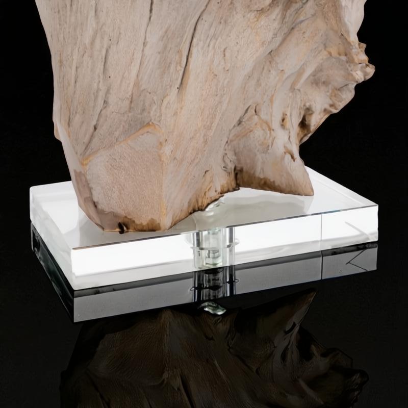 Sculptural wood accent lamp base on a clear glass and black reflective stand.