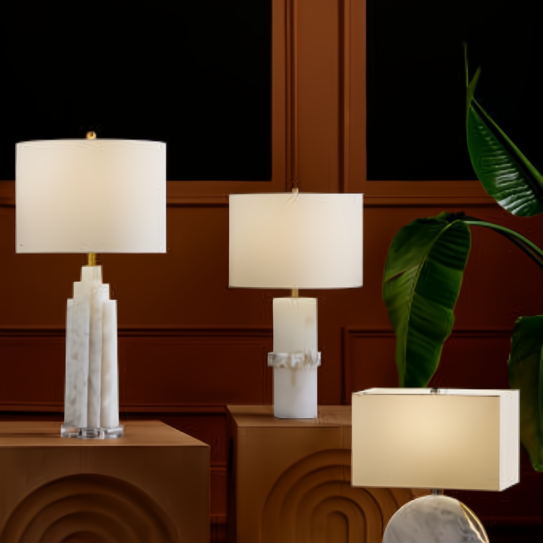 Three unique table lamps, two with white shades and marble bases, one with a rectangular shade, on brown wooden surfaces.