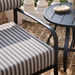 Surya Antibes black powder-coated aluminum round outdoor end table next to a striped patio chair.