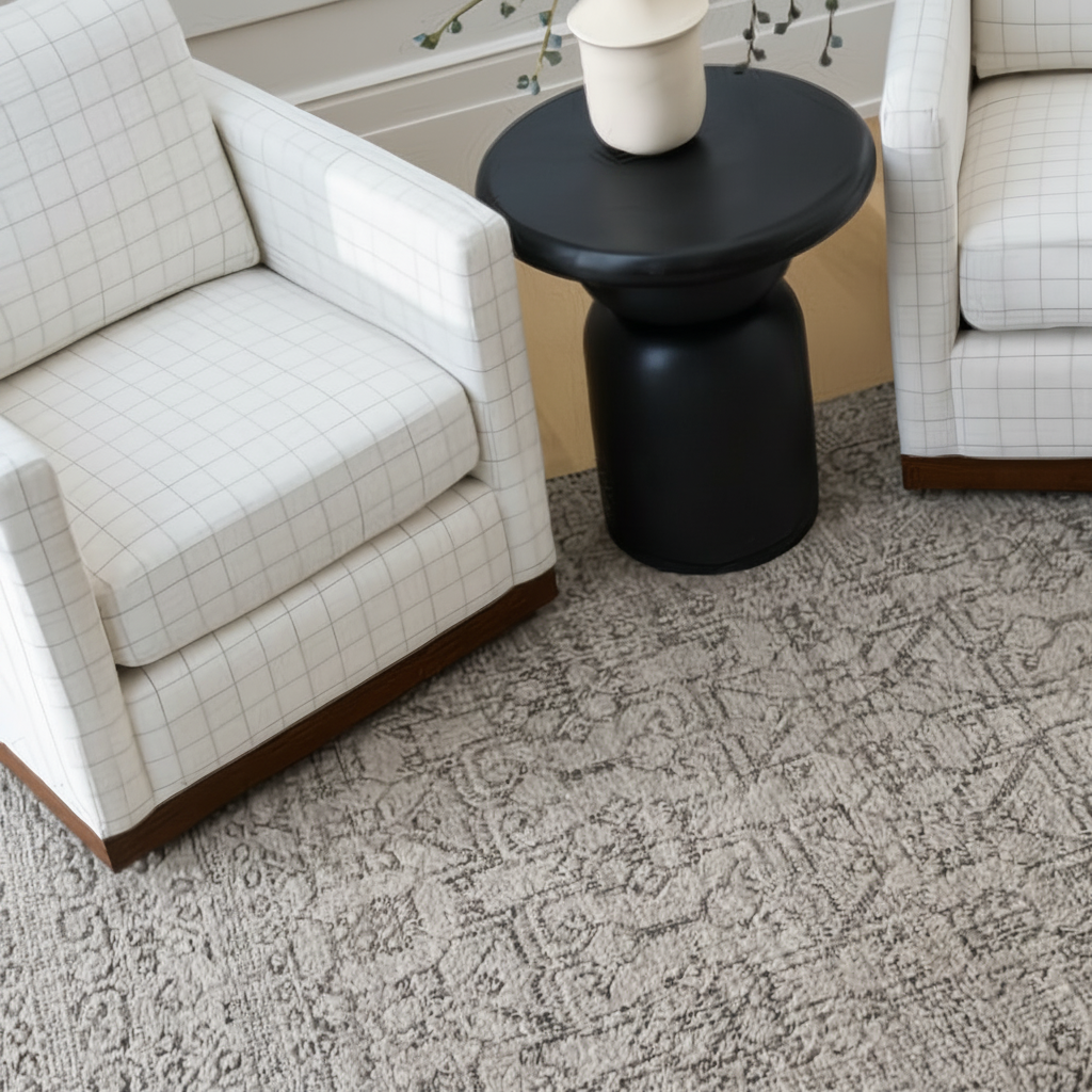 Two light beige grid-patterned Surya Glendon swivel chairs with brown bases flank a black side table on a patterned rug.