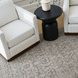 Two light beige grid-patterned Surya Glendon swivel chairs with brown bases flank a black side table on a patterned rug.